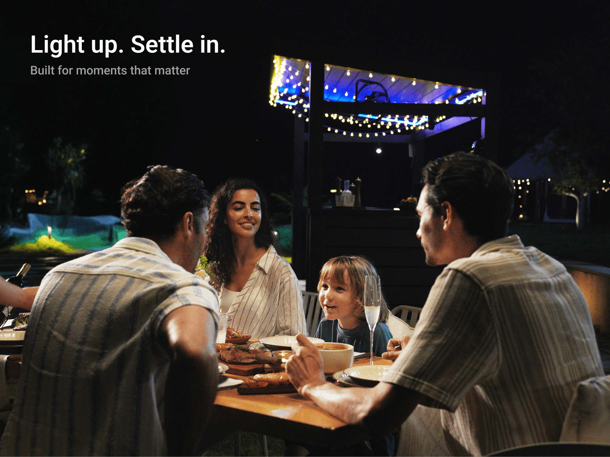 Family dining under LuxPatio louvered pergola with evening string lights and adjustable weather protection.