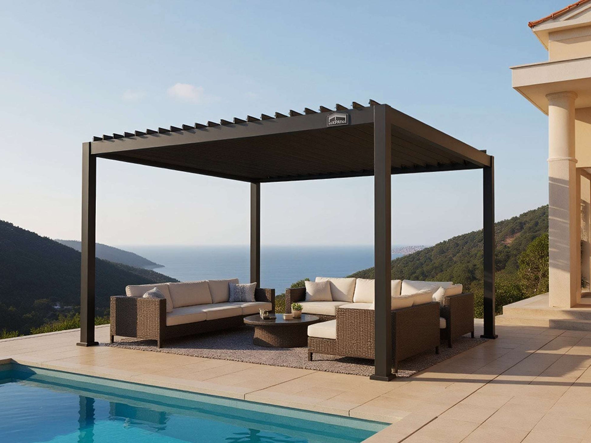 Black LuxPatio aluminum louvered pergola over patio seating area with pool and scenic ocean view backdrop.