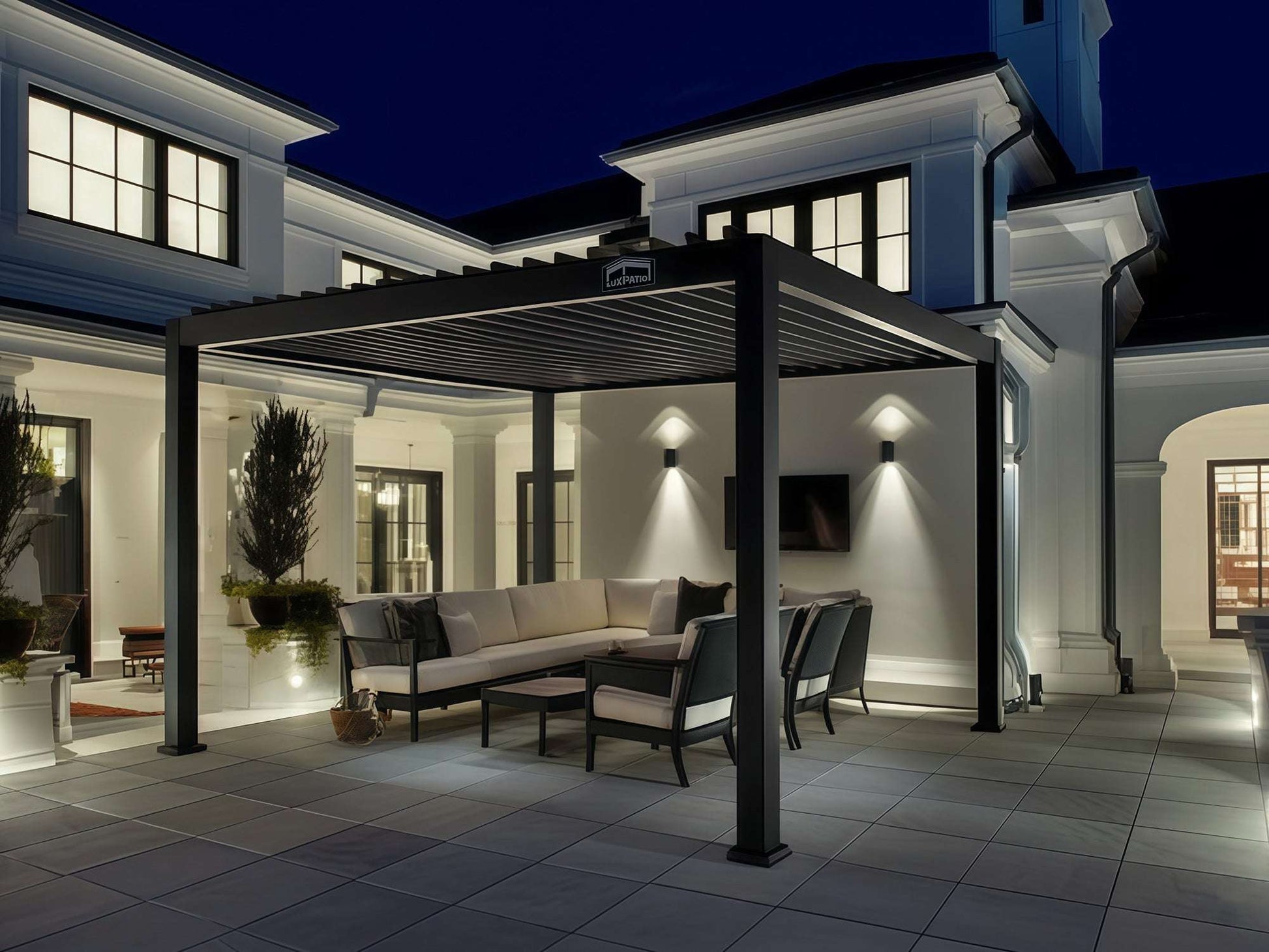LuxPatio black aluminum louvered pergola with seating and lighting, creating an elegant outdoor living space at night.