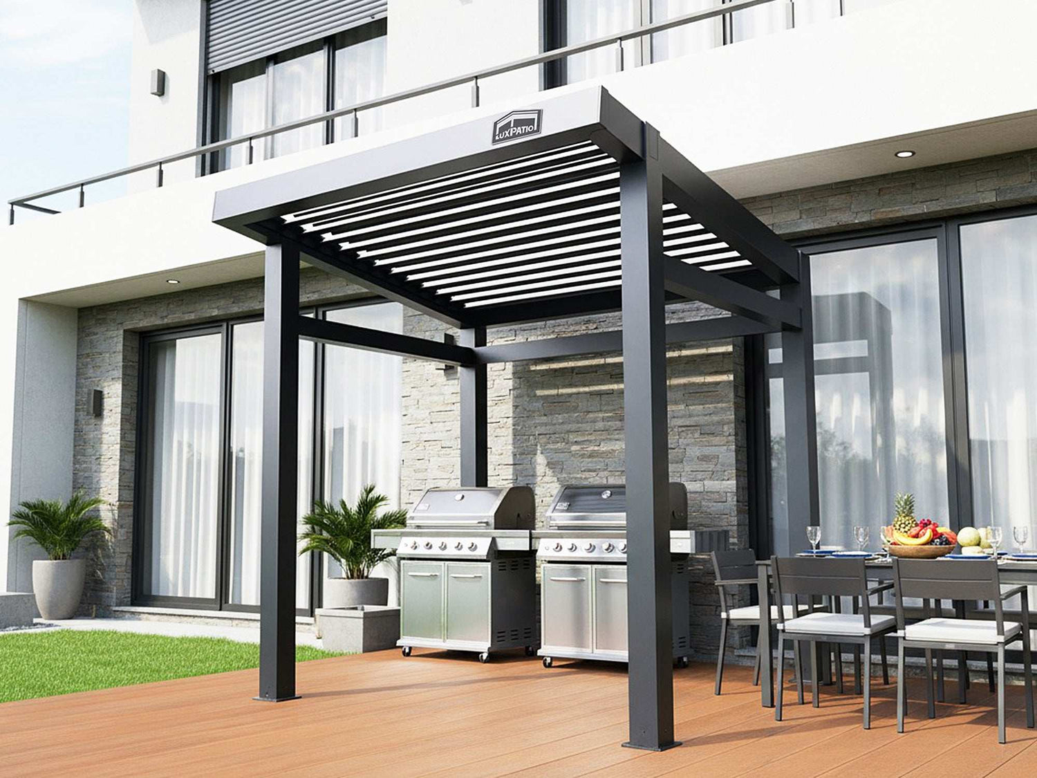 A black louvered pergola covering two large grills and an outdoor dining area on a wooden deck next to a modern building.
