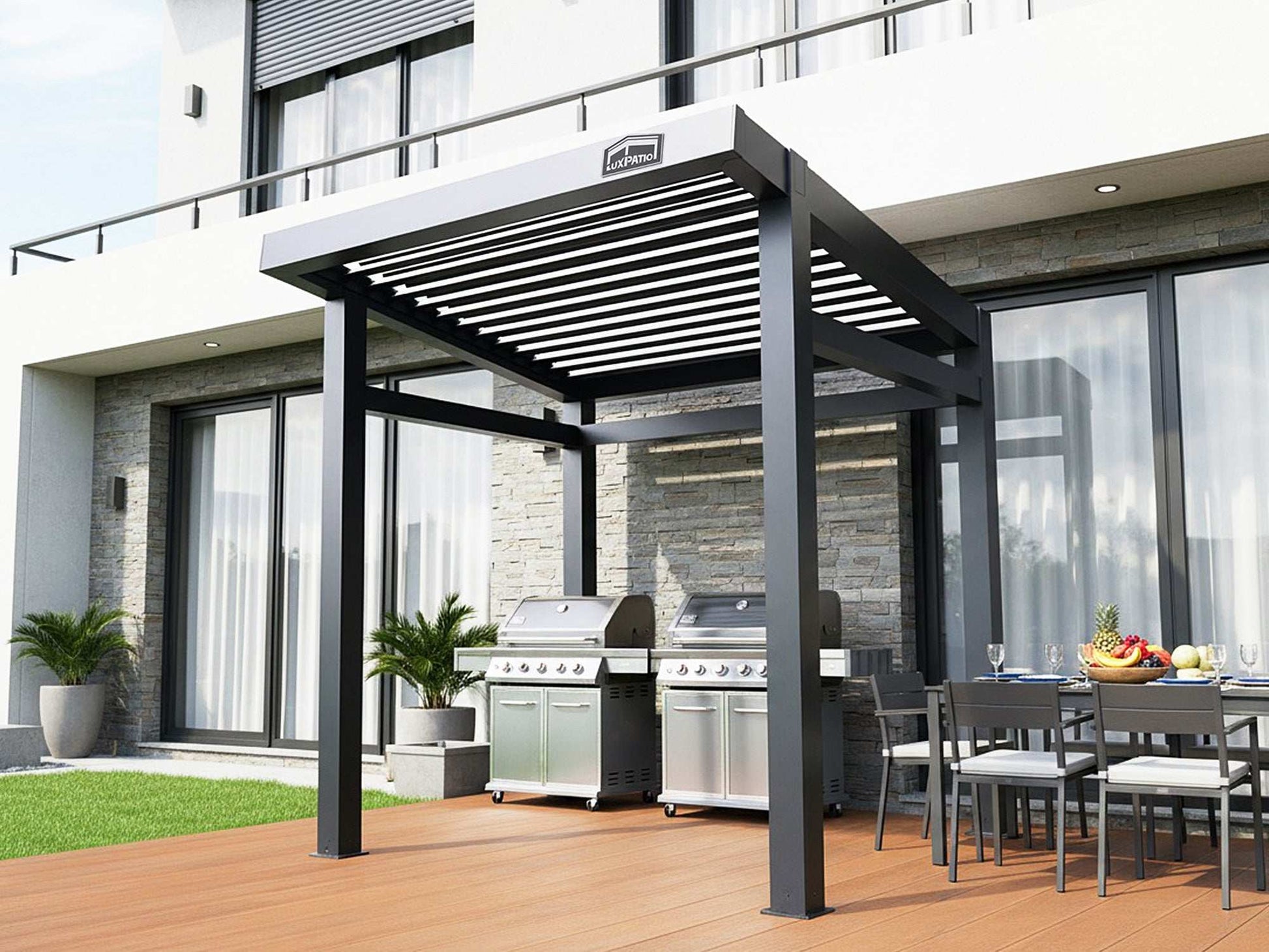 A black louvered pergola covering two large grills and an outdoor dining area on a wooden deck next to a modern building.