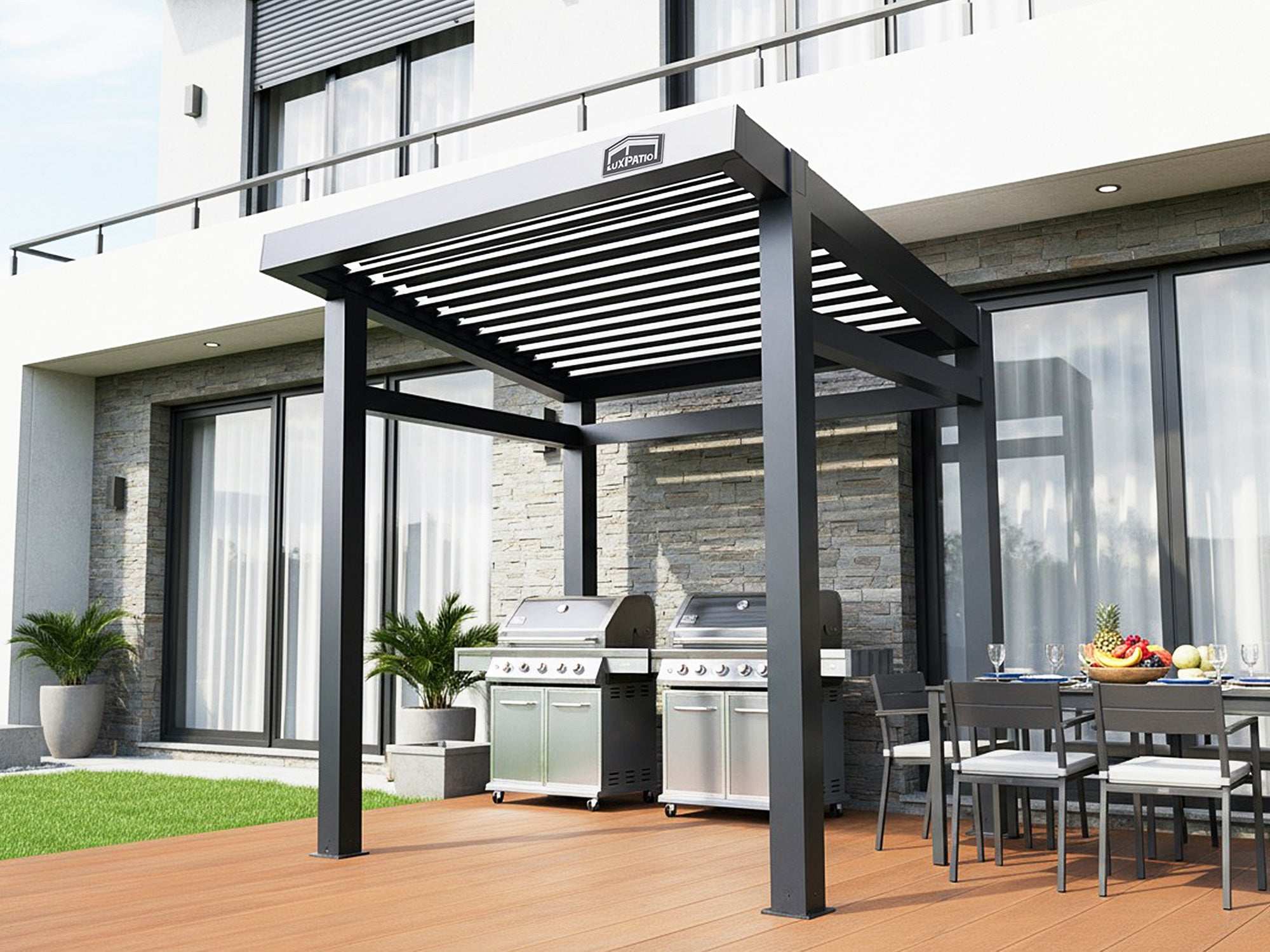A black louvered pergola covering two large grills and an outdoor dining area on a wooden deck next to a modern building.