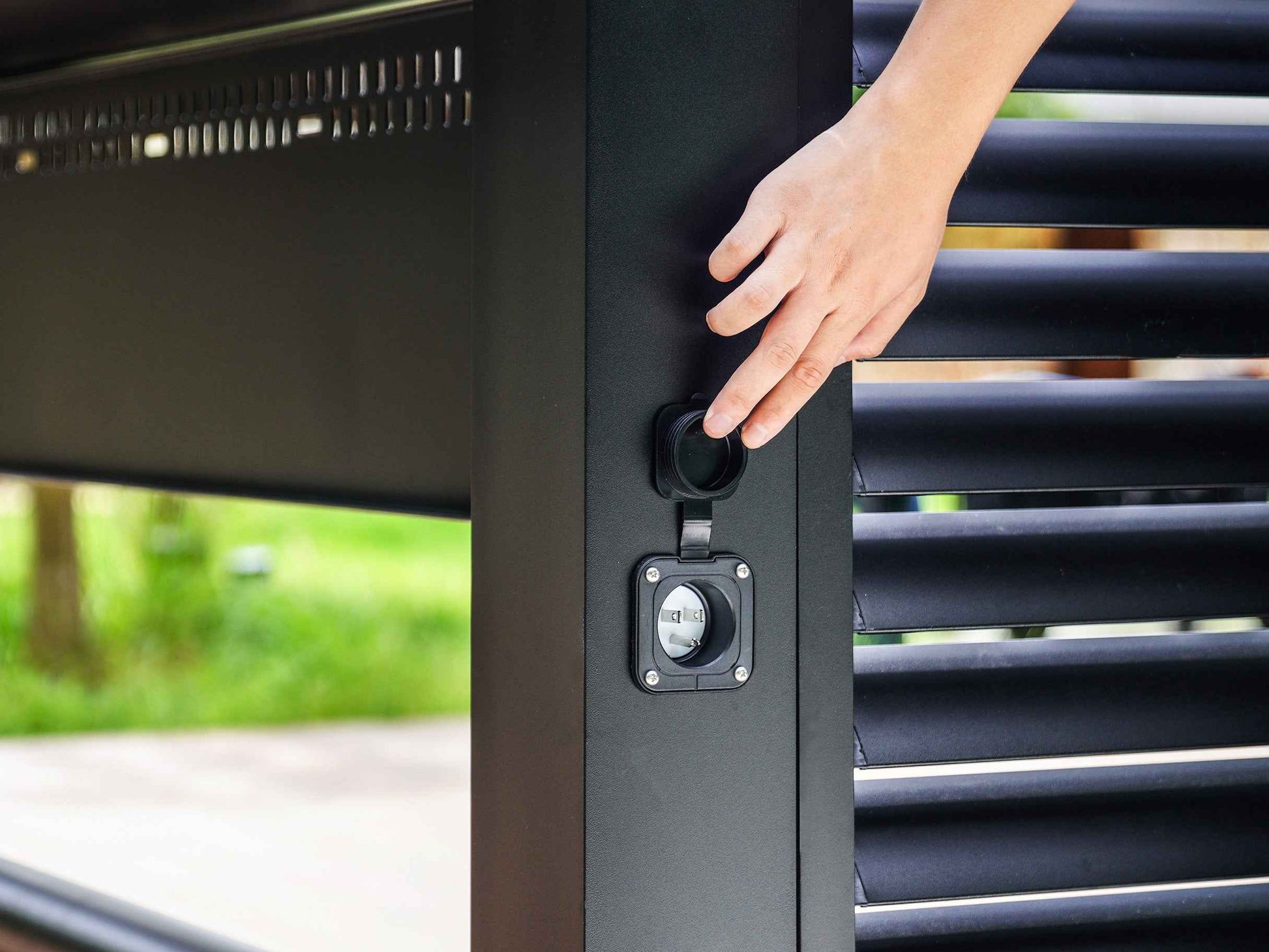 Hand opening weatherproof power outlet cover on Grill Louvered Pergola Pro aluminum construction.
